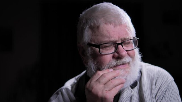 A portrait of a man wearing glasses, gray hair and a beard, lost in thought