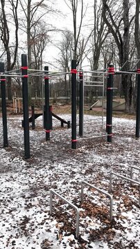 Empty outdoor gym equipment for calisthenics and street workout in a public park during a cold and snowy winter day. No people around