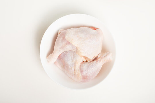 top view of raw chicken legs in white bowl on white background