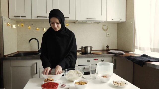 muslim woman in black hijab mixing rice by hand in a white bowl with flour and water on the table during home cooking and baking preparation