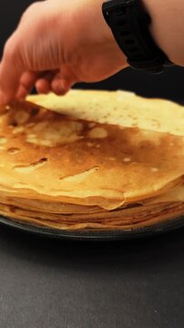 Close up view of a person's hand taking a thin crepe from a stack on a plate. The crepe is folded into quarters against a dark background