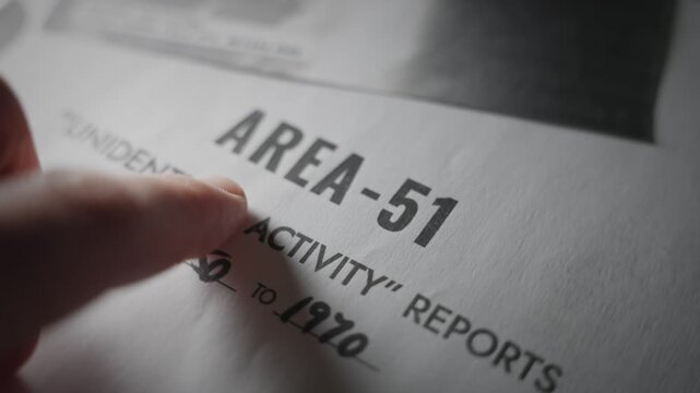 Close up hand pointing on Area 51 report document file folder with UFO activity. Red confidential label stamped on classified top secret report. Evidence and proof of alien extraterrestrial sightings