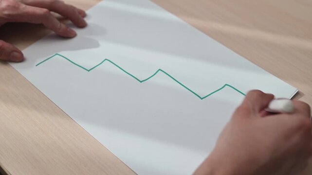 A person draws a line graph on a blank sheet of paper using a marker. This visual can be used in business presentations, educational materials, or financial content