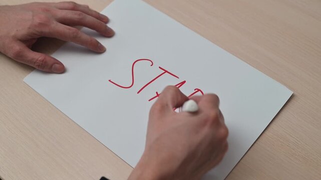 A hand uses a red marker to write the word start on a piece of white paper. The writing process shows multiple angles and emphasizes the action in a workspace environment