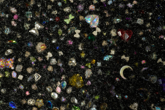 Vibrant mix of colorful sparkling gems, rhinestones, and decorative beads in various shapes creating a magical glowing texture.