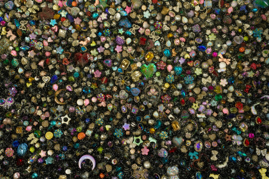 Vibrant mix of colorful sparkling gems, rhinestones, and decorative beads in various shapes creating a magical glowing texture.