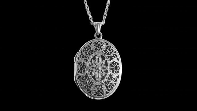 Oval silver locket pendant with intricate filigree floral pattern on a delicate chain, isolated against a solid black background