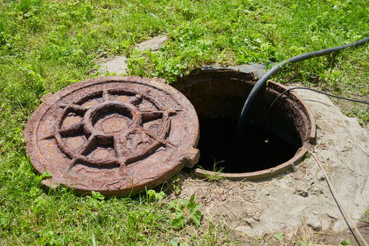 Pumping sewage from septic tank, open rusty manhole and hose pumping out sewage water in backyard