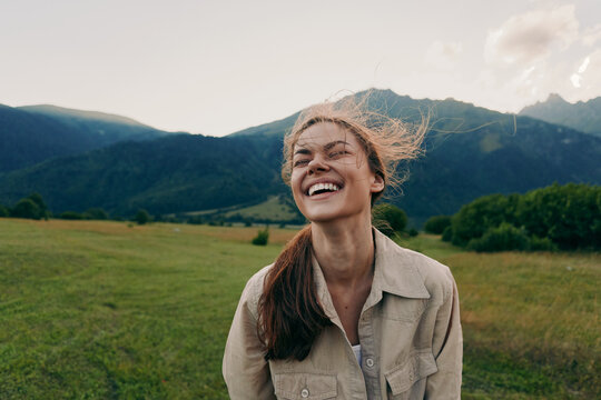 Happy woman enjoying outdoor life, smiling in a grassy field with mountains in the background, casual jacket, sunlit moment, lifestyle portrait of carefree everyday joy