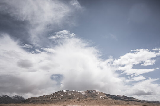 Rocky mountain range with snow and glaciers against a cloudy sky, in the Tien Shan Mountains on Pamirs, stone mountain with red texture, minimalist landscape for background