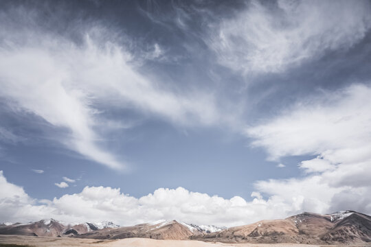 Rocky mountain range with snow and glaciers against a cloudy sky, in the Tien Shan Mountains on Pamirs, stone mountain with red texture, minimalist landscape for background