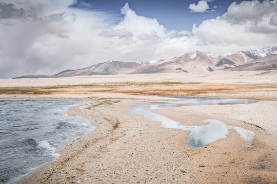 Mountain landscape, a cold high-altitude lake against the backdrop of rocky peaks and ridges with snow and glaciers, a panorama in the Tien Shan Mountains in the Pamirs, a lake with waves