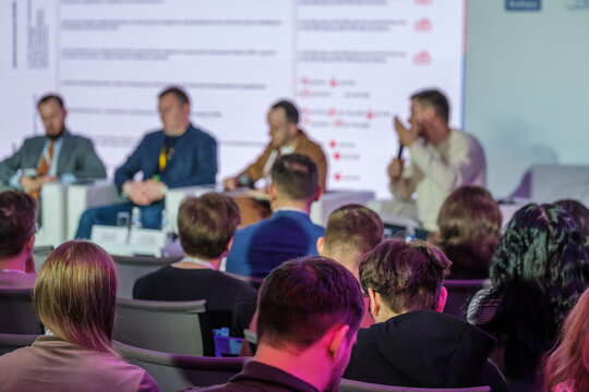 Business panel discussion at conference, audience listens to speakers, professional networking, presentation atmosphere.