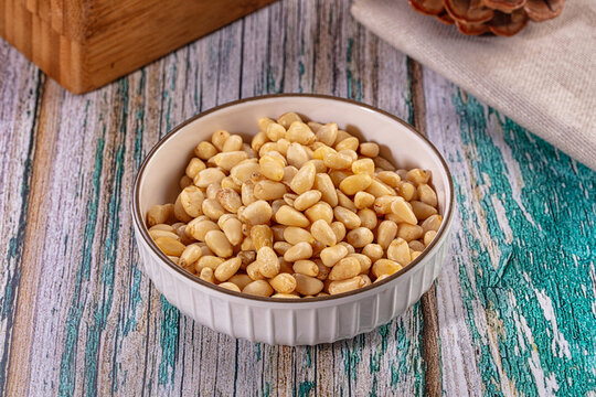 Pine nuts in a white ceramic bowl on a rustic wooden table