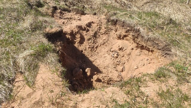 Deep washed out pit in dry grass illustrating Soil erosion concepts. For agricultural warning materials, geology blogs, and terrain damage reports.