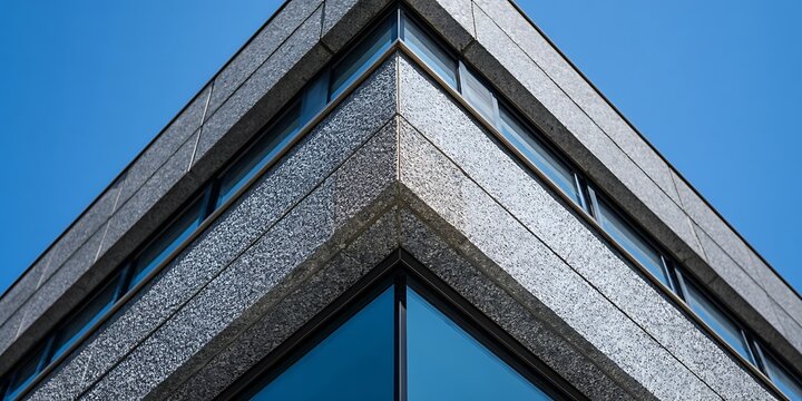 Sharp corner of a modern building with reflective windows against a clear blue sky, viewed from a low angle perspective