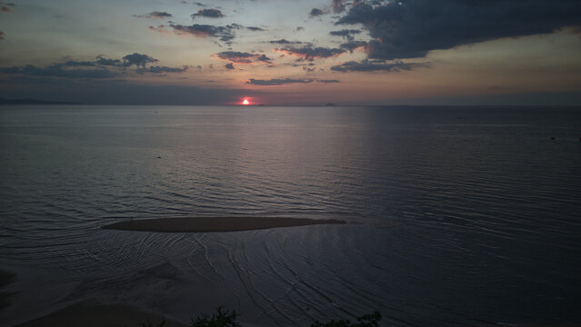 Aerial view of Jomtien Beach at sunset with the sun dipping below the horizon over the calm sea and a small sandbar in the foreground Chon Buri, Thailand.
