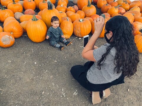Rear view of a woman kneeling on the ground taking a photo of her son in front of a freshly harvested pumpkins, Draper, Utah, USA