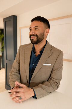 Portrait of a smiling businessman in a suit standing next to a high-top table looking sideways