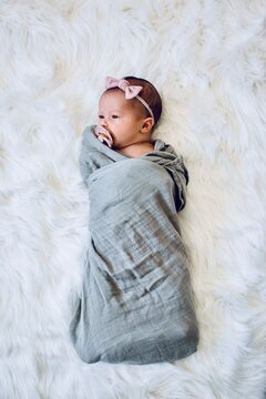 Overhead view of a newborn Baby Girl wrapped in a blanket wearing a hairband sucking on a pacifier