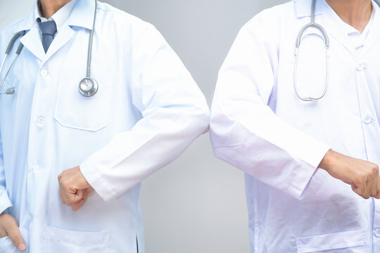 Close-up of two doctors in laboratory coats and stethoscopes greeting each other by bumping elbows