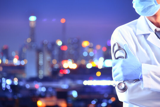 Close-up partial portrait of a doctor wearing a laboratory coat and protective workwear standing in front of an illuminated cityscape at night