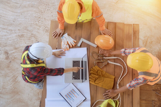 Overhead view of a three construction workers standing around a table looking at construction plans and a laptop, Thailand