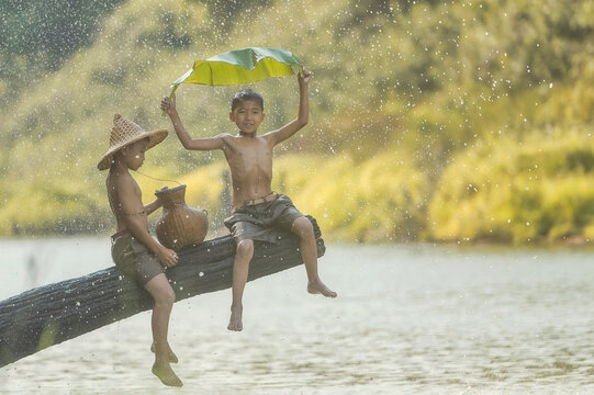 Two Happy boys in wet shorts sitting on a log by a river, Thailand