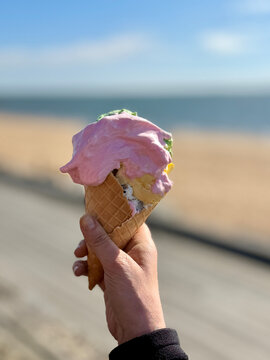 Close-up of a woman standing by the sea holding a traditional Danish ice cream cone with marshmallow fluff on a sunny spring day, Hjerting, Esbjerg, Jutland, Denmark