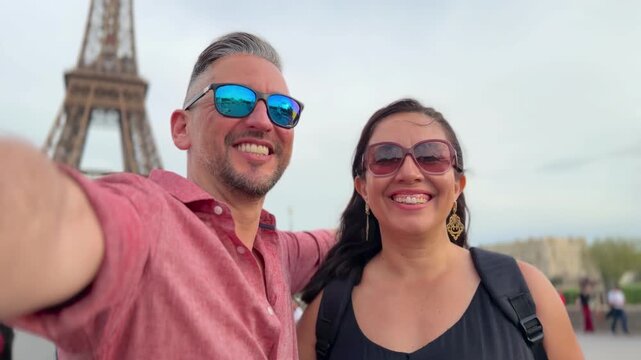 Smiling couple on the Eiffel Tower observation deck, raising arms and taking a selfie while enjoying panoramic Paris views, romance and joyful urban travel celebration