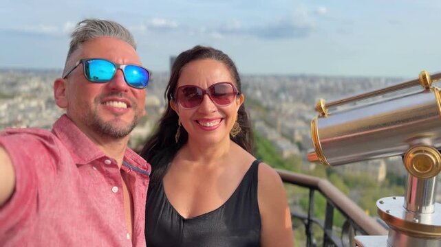 Smiling couple on the Eiffel Tower observation deck, raising arms and taking a selfie while enjoying panoramic Paris views, romance and joyful urban travel celebration