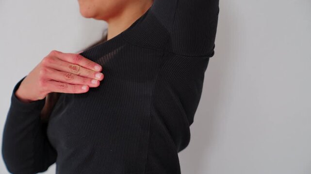 Woman feeling uncomfortable raising arm with visible sweat stain on her black shirt due to hyperhidrosis.