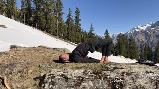 advanced yoga backbend chakrasana on rocky ground with snow covered slopes