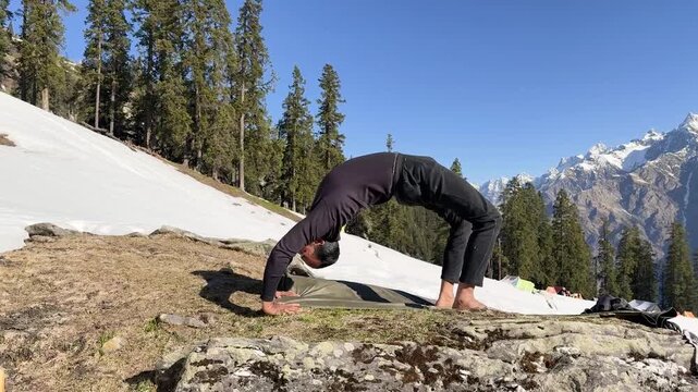 yoga practice in nature with man performing backbend on snow covered hillside