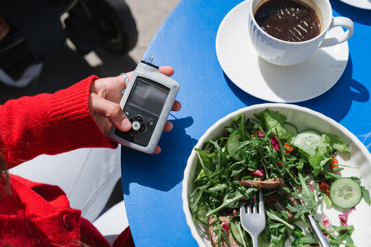 Overhead view of a diabetic woman sitting at a table with a cup of black coffee and roast beef salad using an insulin pump