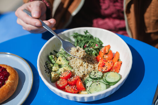 Close-up of a man sitting outdoors on a sunny day eating a healthy quinoa salad with fresh avocado, cucumber, tomato, red pepper and rocket