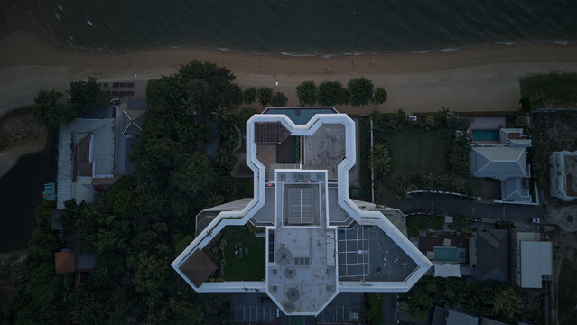 Aerial view of Jomtien Beach with a modern geometric building rooftop, lush tropical trees, and sandy shoreline Chon Buri, Thailand.