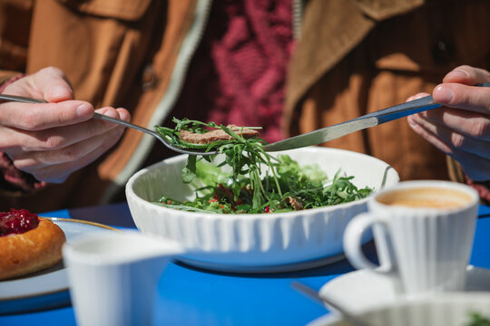 Close-up of a man sitting at an outdoor cafe enjoying a roast beef salad, cherry pastry and coffee