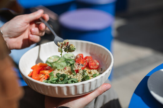Close-up side view of a man sitting outdoors on a sunny day eating a healthy quinoa salad with fresh avocado, cucumber, tomato red pepper and rocket
