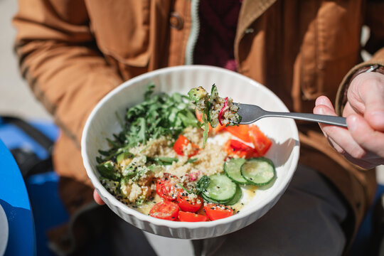 Close-up of a man sitting outdoors on a sunny day eating a healthy quinoa salad with fresh avocado, cucumber, tomato, red pepper and rocket