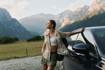 Fototapeta premium Young woman in casual outfit leaning on car outdoors with mountains in background. Concept of lifestyle, travel, freedom, and adventure in nature.