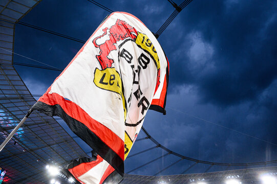 Bayer 04 Leverkusen supporter flag waving inside the stadium under dramatic dark clouds, matchday atmosphere in Germany.