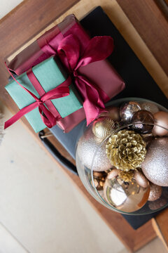 Still-life showing stacked teal-burgundy gifts on tray with glass bowl of gold pinecone and baubles