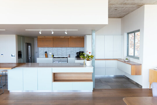 Large central island anchoring modern kitchen, showing pale countertop, wooden shelf, potted plant