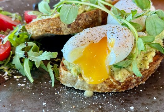 Close-up of two slices of avocado toast with poached eggs and salad