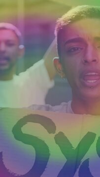 Vertical video: Two men lip-syncing to camera holding protest sign, rainbow wash across faces