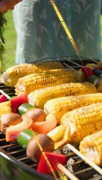 Vertical video: Woman tending barbecue taking bowl, basting corn and skewers for flavor