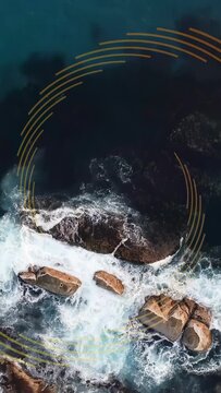 Vertical video: Drone descending while gold arcs rotating, waves breaking, showing rocks for design