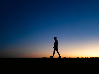 Fototapeta premium Silhouette of a man walking alone at sunset or sunrise with a colorful sky