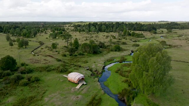 Low-altitude drone tracking shot moving from left to right, showing a prehistoric hut replica and the Chinchihuapi stream at Monte Verde, Chile.